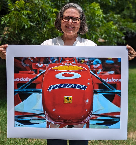 A woman holding up a painting of a Shan Fannin | "Ferrari F2002" | 25 x 32" racing car.