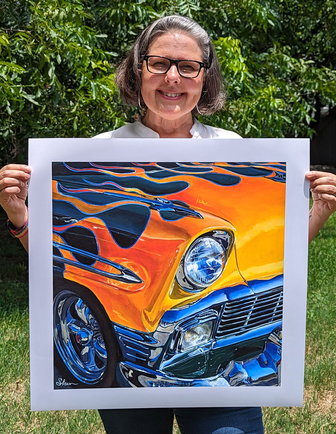 A woman holding up a painting of the "Flamin’ Chevrolet Bel Air" by Shan Fannin, measuring 28 x 28".
