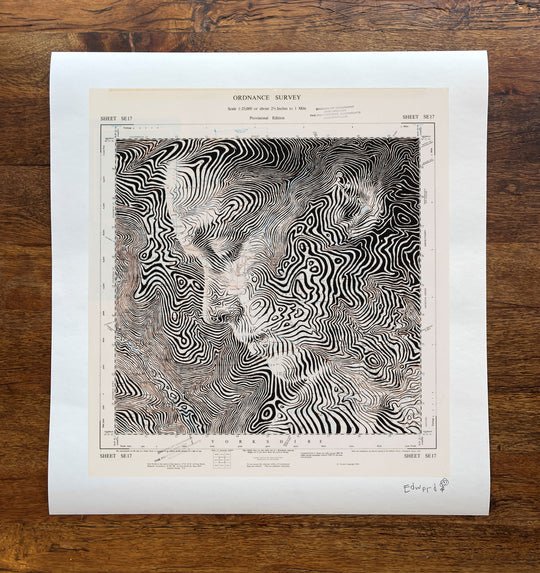A print of a woman's face on a wooden table, created by Ed Fairburn in the United Kingdom, featuring Fountains Earth.